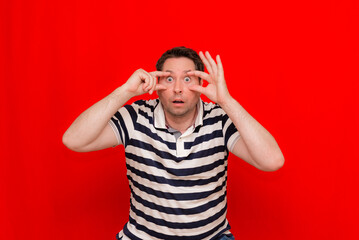 American 30s man wearing casual striped t-shirt standing over isolated red background. Pointing to the eye