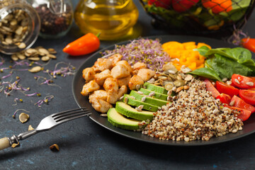 Salad with quinoa, avocado and chicken. Front view. Served on a black plate.