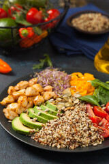 Salad with quinoa, avocado and chicken. Front view. Served on a black plate.