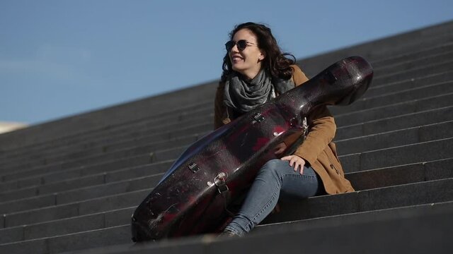 Mujer sentada con su violonchelo en una escalera
