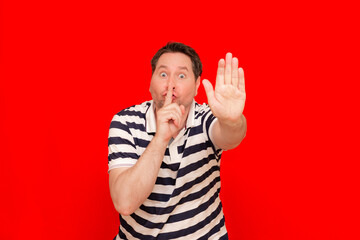Fototapeta premium Glad mysterious male bee belly model shows silence sign or hush gesture.red background