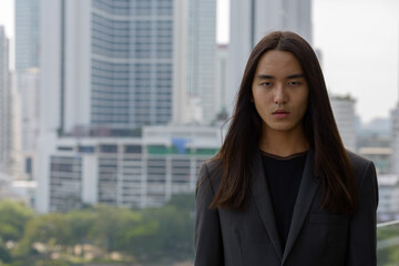 Young Asian businessman with long hair in the city outdoors