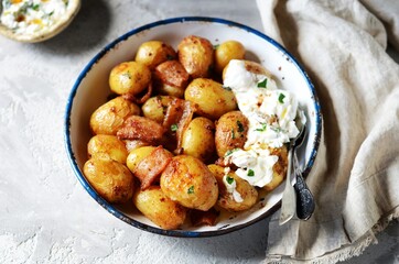 Baked young potatoes with bacon and sour cream sauce on a gray background, still life