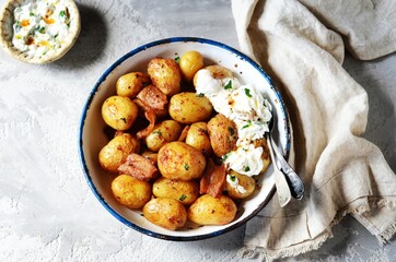 Baked young potatoes with bacon and sour cream sauce on a gray background, still life