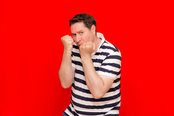 Confused 35s man wearing striped t-shirt over isolated red background Punching fist to fight, aggressive man