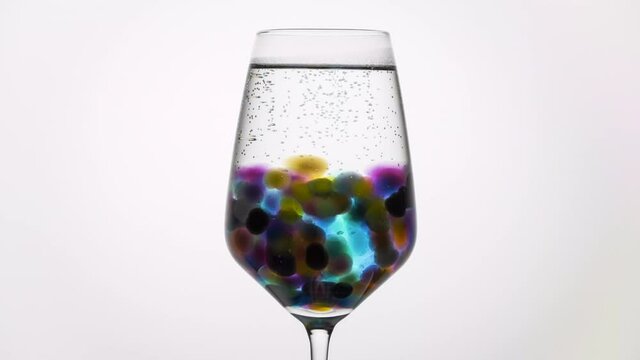 A timelapse of coloured orbeez, aka hydrogel, expanding in a glass of water against a white background