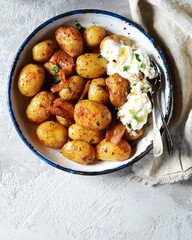 Baked young potatoes with bacon and sour cream sauce on a gray background, still life