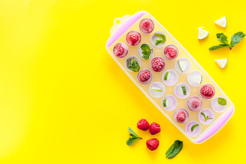 Ice tray with berries, lime and mint on yellow background top view copy space