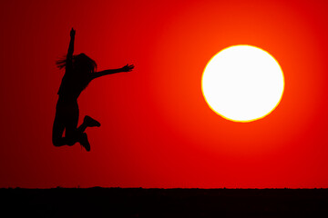 Young girl jumps high in joy. At sunset, the silhouette of his body is visible. The concept of nature and beauty. Orange sunset. Girl silhuette at sunset.