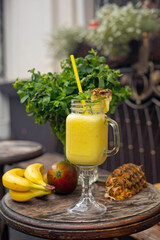 Cool smoothie with pineapple, mango, banana and mint on wooden background
