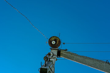 Old rusty lantern on an electric pole with wires, against a clear blue sky.