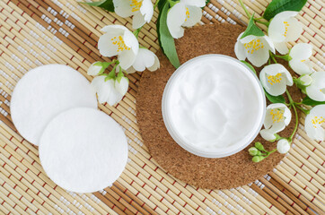 White facial mask  (face cream, hair mask, body butter, facial cleanser) in the small white jar, cotton pads and jasmine flowers. Natural skin and hair concept. Top view, copy space.