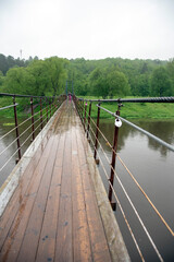 Wooden suspension bridge over the river on a rainy day.