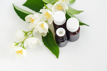 Obraz na płótnie Canvas Small glass bottles with essential jasmine oil (tincture, infusion, perfume) on the white background and jasmine flowers. Aromatherapy, spa and herbal medicine ingredients. Top view, copy space.