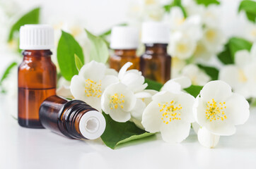 Obraz na płótnie Canvas Small glass bottle with essential jasmine oil (tincture, infusion, perfume) on the white background. Jasmine flowers close up. Aromatherapy, spa and herbal medicine ingredients. Copy space.