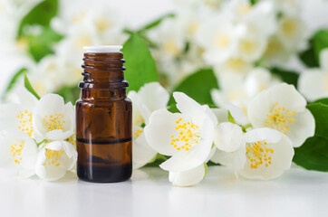 Small glass bottle with essential jasmine oil (tincture, infusion, perfume) on the white background. Jasmine flowers close up. Aromatherapy, spa and herbal medicine ingredients. Copy space.