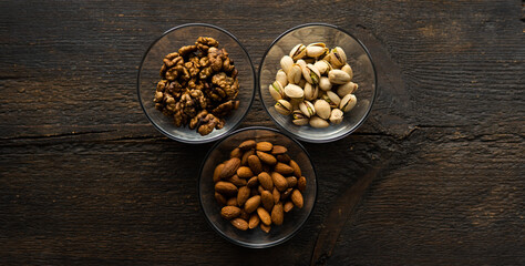 Almond, pistachio and walnut in a small plates which standing on a vintage wooden table. Nuts is a healthy vegetarian protein and nutritious food.