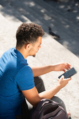 behind young mixed race man sitting on steps looking at mobile phone