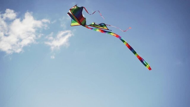 Multi-colored bright kite flying in the blue sky in summer in slow motion