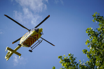 The air ambulance, service arrives at the scene of an accident. Flying yellow medical ambulance helicopter over the trees. Background of blue sky with clouds. Pest county / Hungary - 06/01/2020