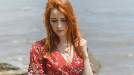 Redhead woman in dress enjoys a walking near the sea shore.