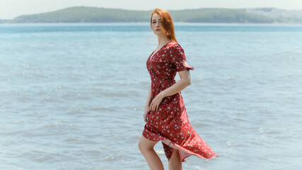 Redhead woman in dress enjoys a walking near the sea shore.