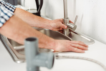 Naklejka premium Selective focus of plumber fixing kitchen faucet near pipes on worktop