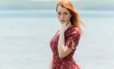 Redhead woman in dress enjoys a walking near the sea shore.