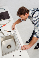 High angle view of plumber using industrial measuring tape near sink and tools on kitchen worktop