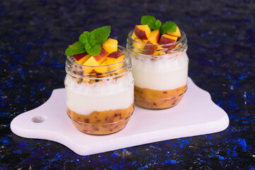 Yogurt with peach and granola in jars on a blue background.