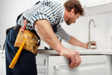 Fototapeta na wymiar Selective focus of plumber in tool belt repairing kitchen faucet