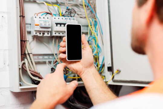 Selective focus of electrician holding smartphone near electrical distribution box