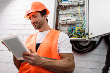 Selective focus of handsome electrician using digital tablet near electrical distribution box
