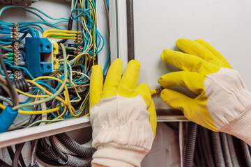 Cropped view of electrician in gloves holding wire near electric panel