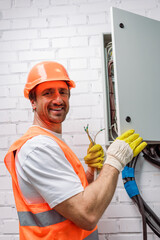 Side view of electrician in hardhat smiling at camera while holding wires near electrical...