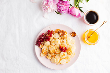 Tiny pancakes with berries, honey, flowers, coffee. Pancake cereal. The concept of Breakfast, food trends. Copy space.