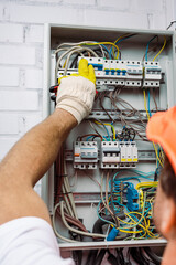 Selective focus of electrician in glove holding pliers and turning on toggle switches of electrical...