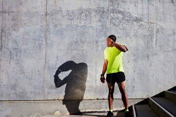 Tired sportsman in fluorescent t-shirt rubbing his forehead resting after a morning jogging while standing against cement wall background with copy space area for your text message or content