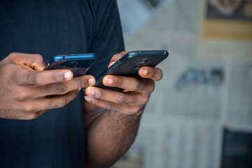 closeup of a young african man using two mobile phones simultaneously