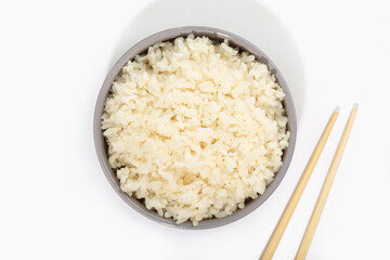 Cooked rice in bowl with chopsticks on white background. Top view