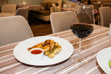 Served delicious food in the restaurant, salads, dishes, meat, sauces. Chicken with a delicious crust with potatoes and sauce.  A glass of red wine.
