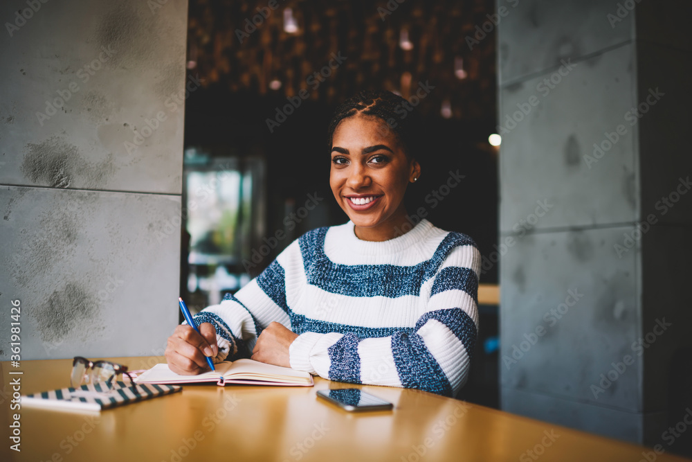 Poster half length portrait of successful afro american student smiling at camera while preparing homework 