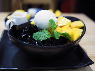 A colorful tasty sliced ripe mango, coconut milk ice cream and grass jelly cubes on black plate served with Thai tea. selective focus.