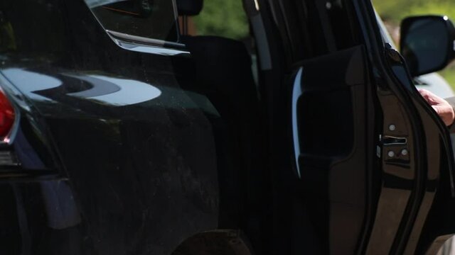 male hand opens the door of a black business class car. Silhouette of a woman in an elegant dress gets into a car