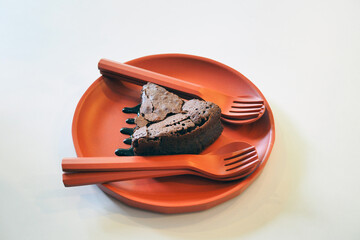 A plate of chocolate brownie cake with soft crusted texture surface, decorated with chocolate sauce served  with spoon and fork on  wooden orange plate.