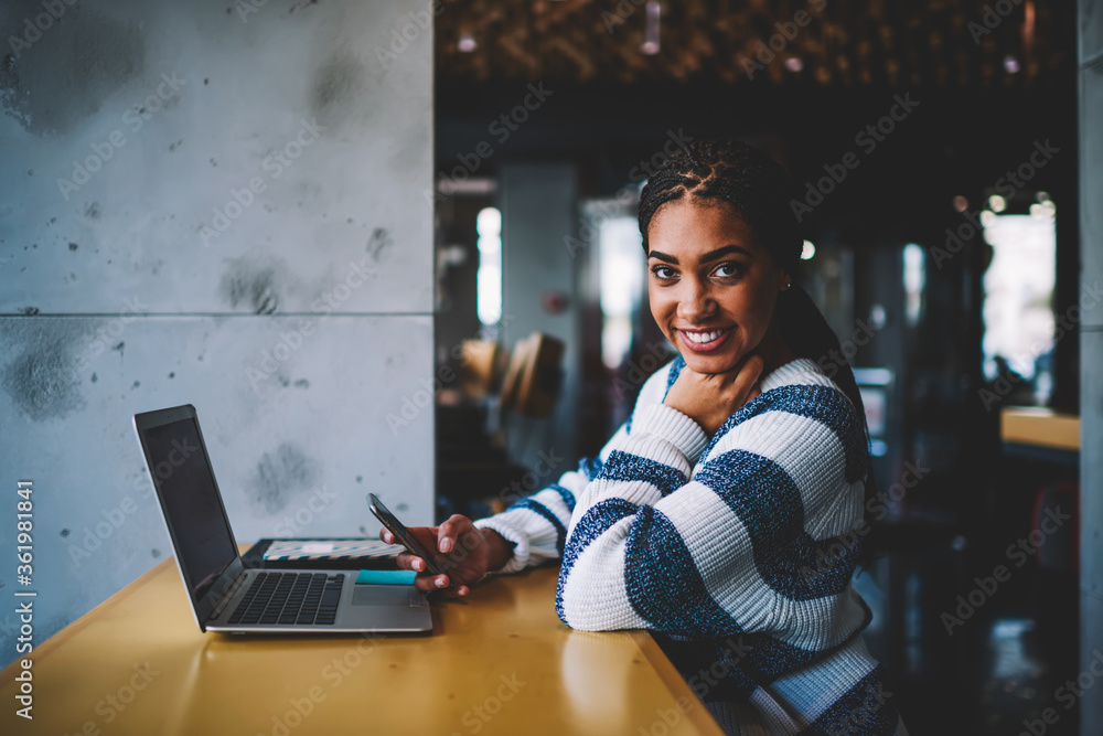 Poster half length portrait of successful afro american blogger smiling at camera while installing mobile a