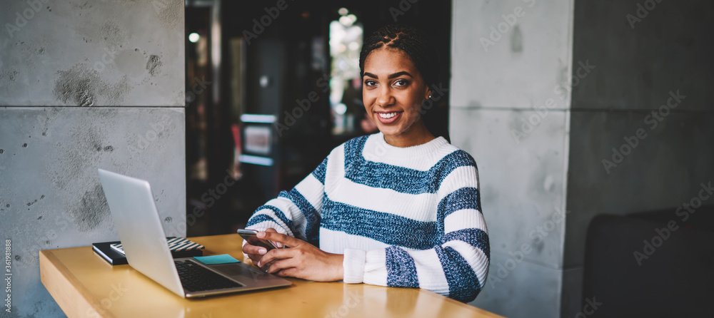 Poster portrait of happy hipster girl smiling and looking at camera and holding smartphone gadget in hands 