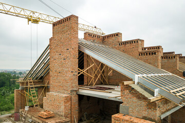 Fototapeta premium Aerial view of unfinished brick apartment building with wooden roof structure under construction.