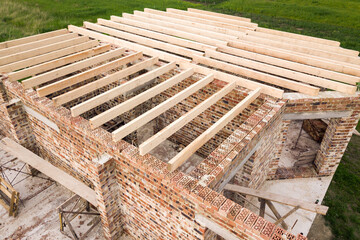 Close up of a brick house with wooden ceiling frame under construction.