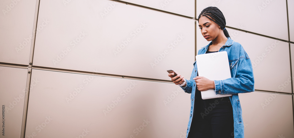 Poster serious female student with laptop computer in hands reading incoming message from colleague using 4